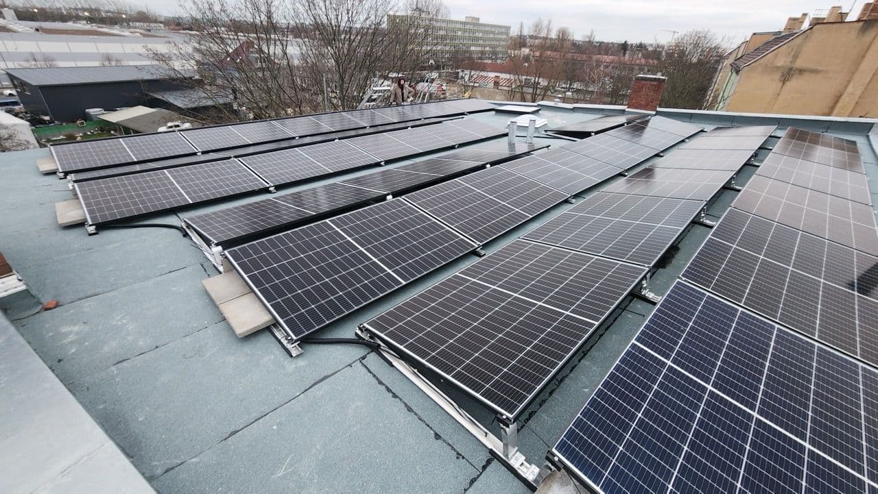 Mehrere Reihen Solarpaneele sind auf einem Dach zu sehen. Dahinter Bäume ohne Laub und weitere Häuser