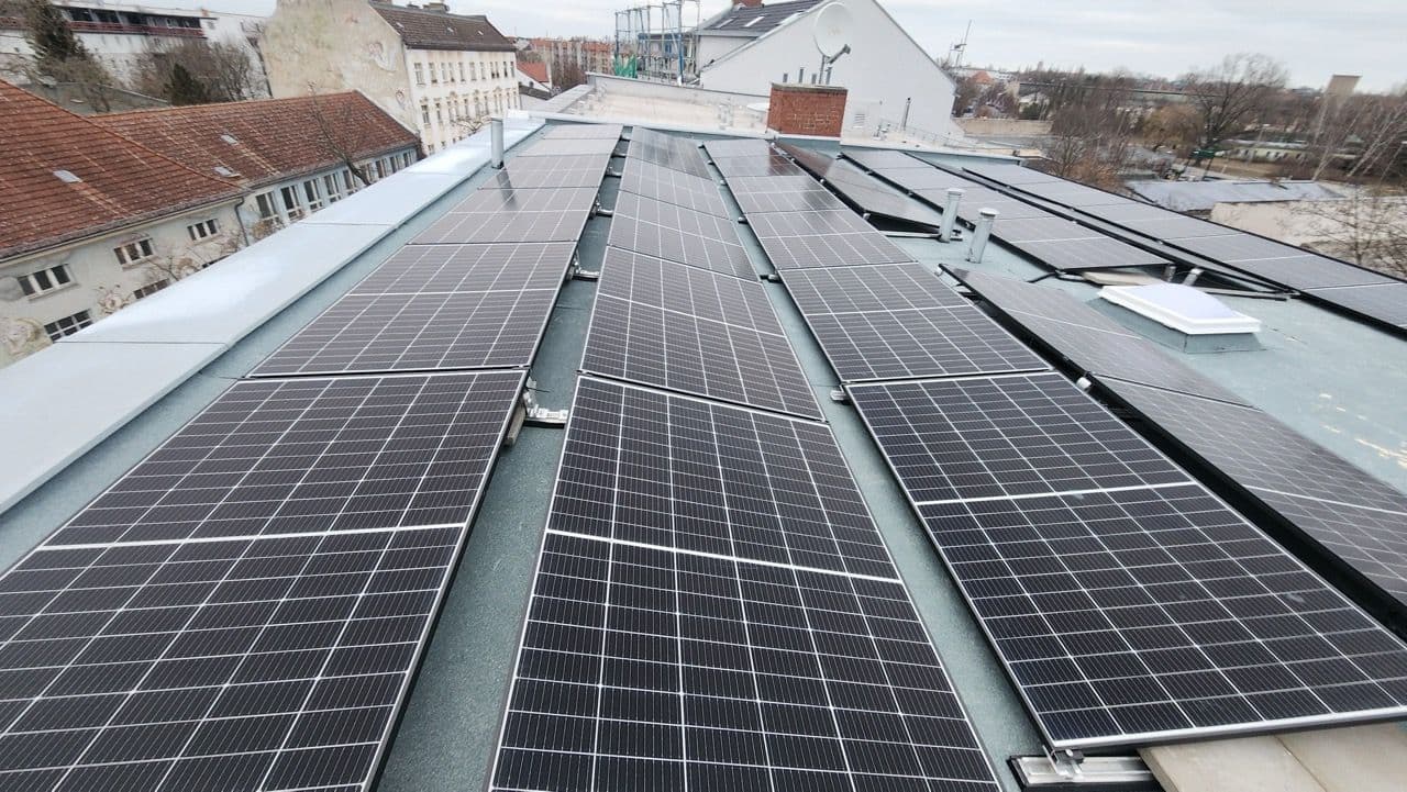 Drei Reihen PV Module auf einem Dach in Berlin. Im Hintergrund Hause und einige Bäume ohne Laub 