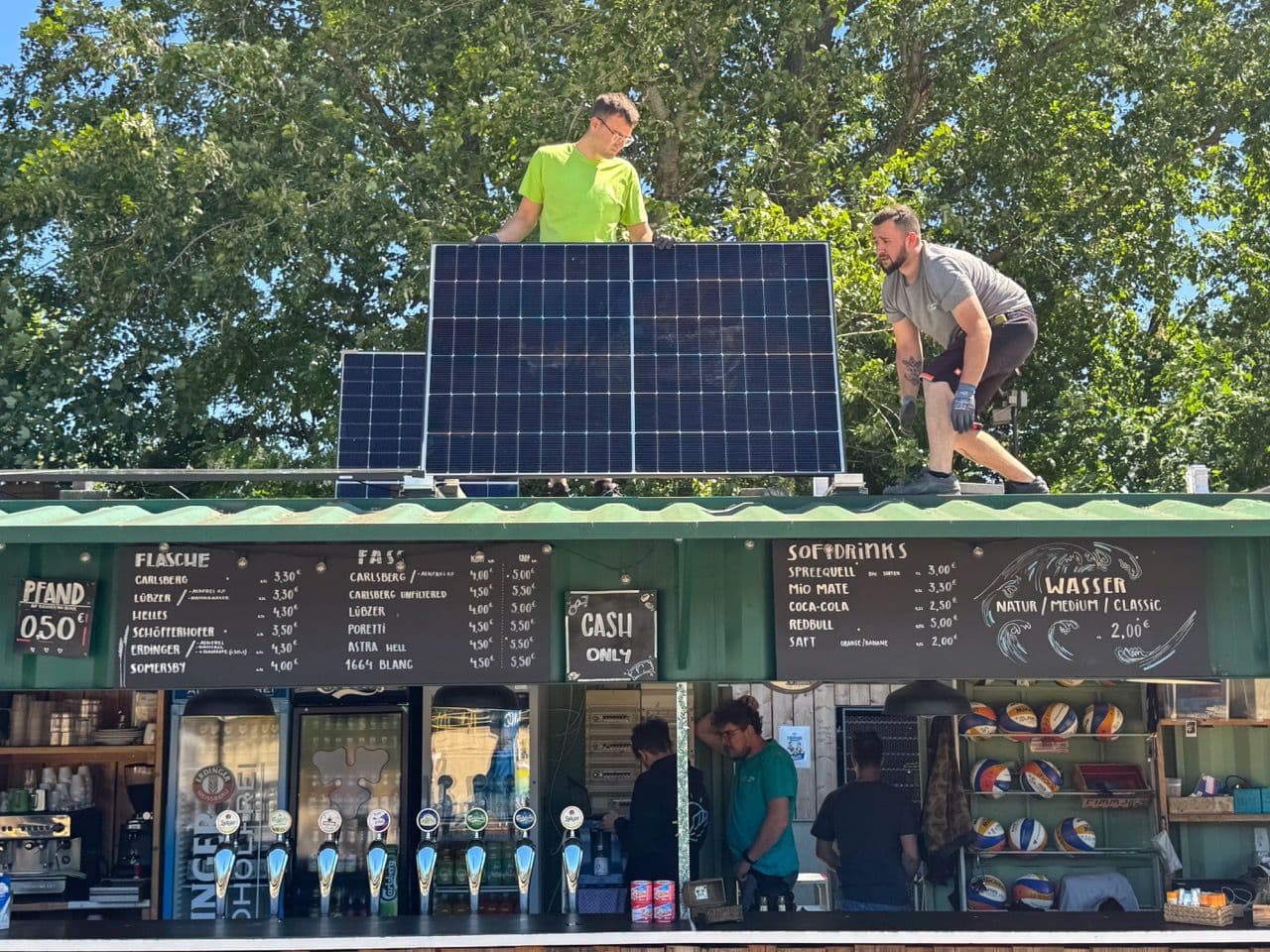Zwei Monteure des Berliner Photovoltaik Fachbetriebs sunday solar montieren ein Solarpanel auf die Bar des Beachvolleyball Platzes Beach61