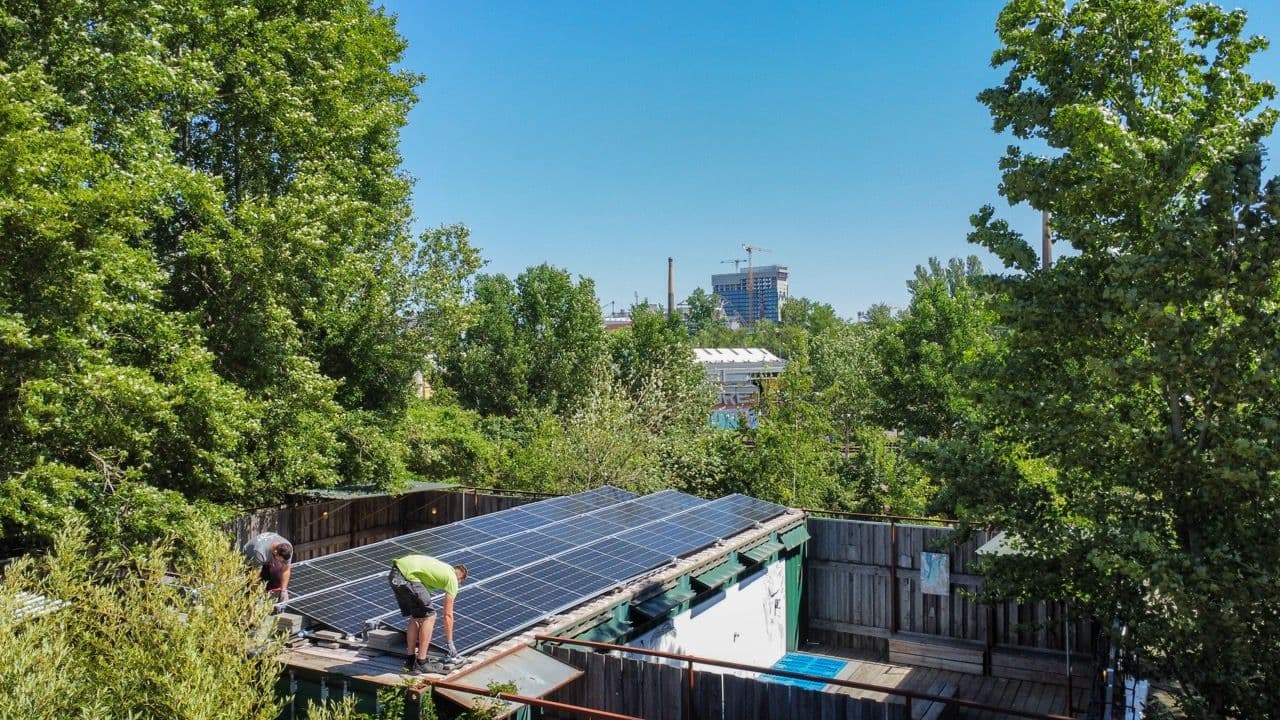 Aus der Ferne sehen wir zwei Mitarbeiter von sunday solar, die eine PV Anlage verbauen. Rundherum Bäume