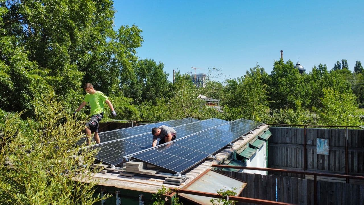 Zwei Monteure von sunday solar fixieren Solarmodule auf einem Dach im Grünen