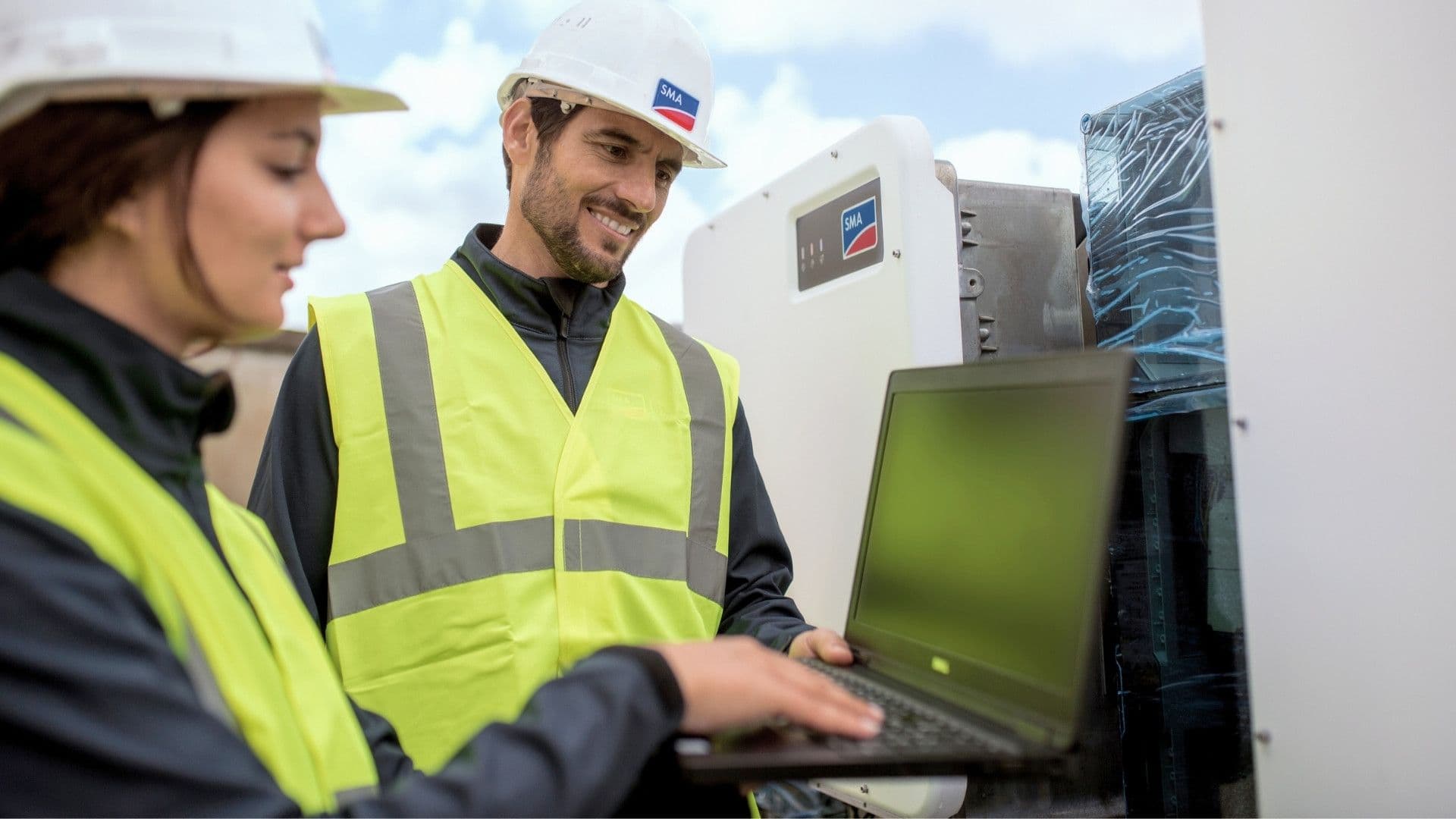 Zwei Mitarbeiter der Firma SMA in Warnwesten schauen auf einen Laptop Screen | sunday solar findet das passende Energiemanagement System für Sie