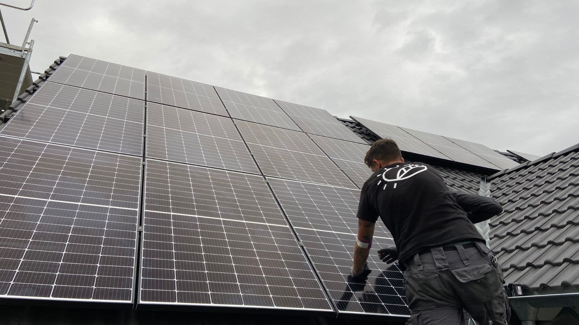 Ein Mitarbeiter von sunday solar fixiert ein Solar-Paneel auf einem Dach. Der Himmel ist grau.
